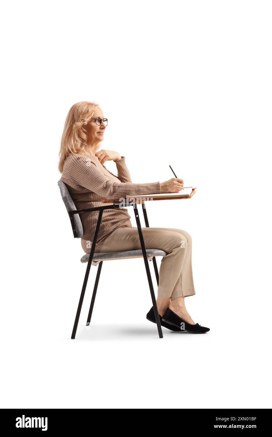 Donna seduta su una sedia scolastica e a scrivere isolata su sfondo bianco Foto Stock