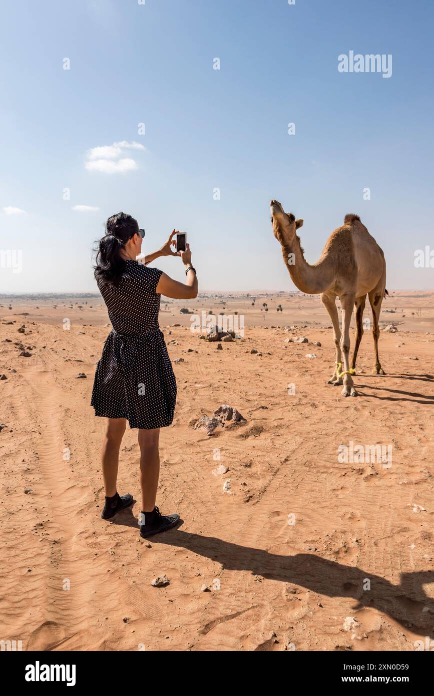 Donna che fotografa un cammello nel deserto, catturando l'essenza dell'avventura e dell'esplorazione Foto Stock