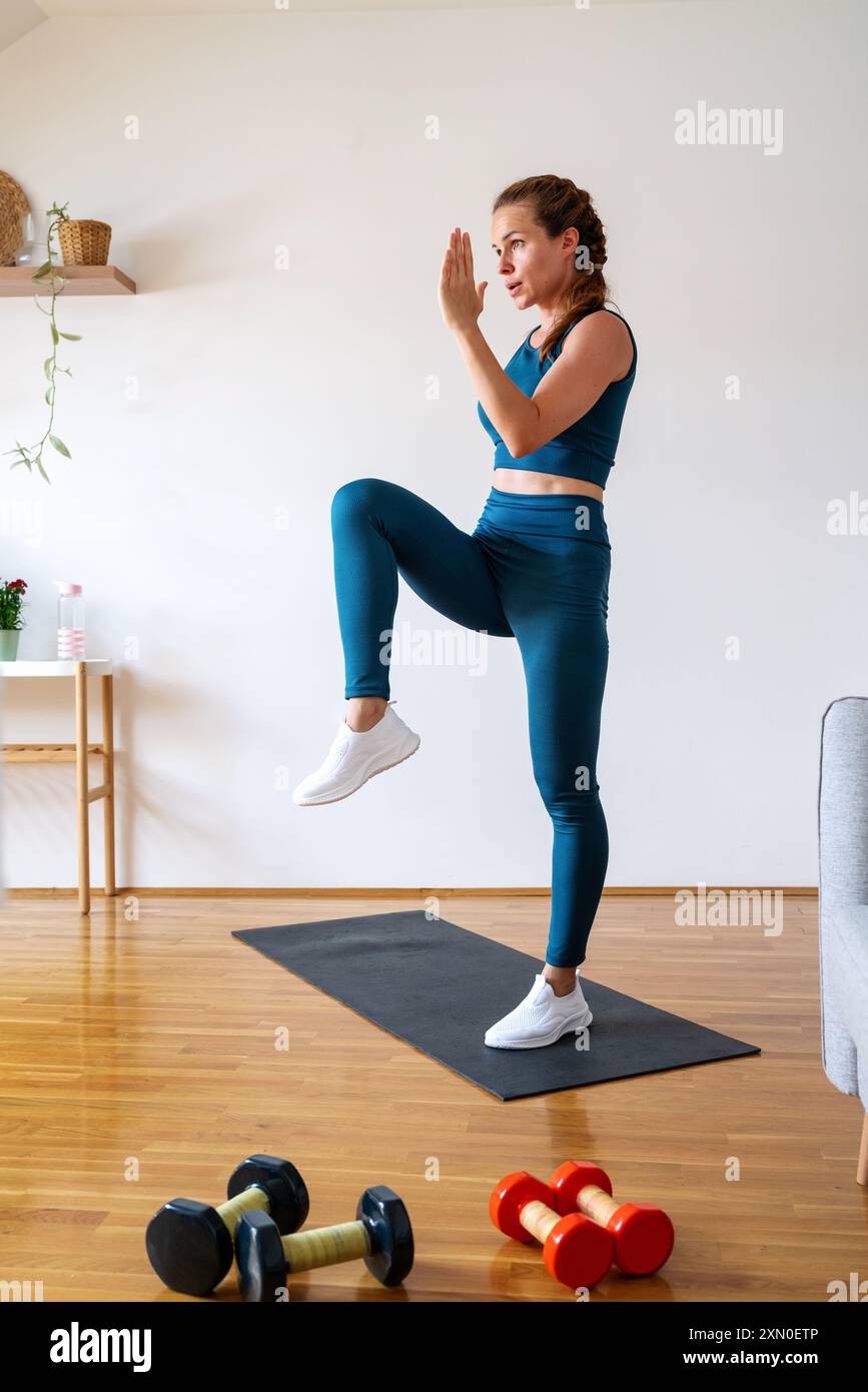 Donna caucasica atletica che indossa abbigliamento sportivo e fa esercizio anaerobico a casa. Foto Stock