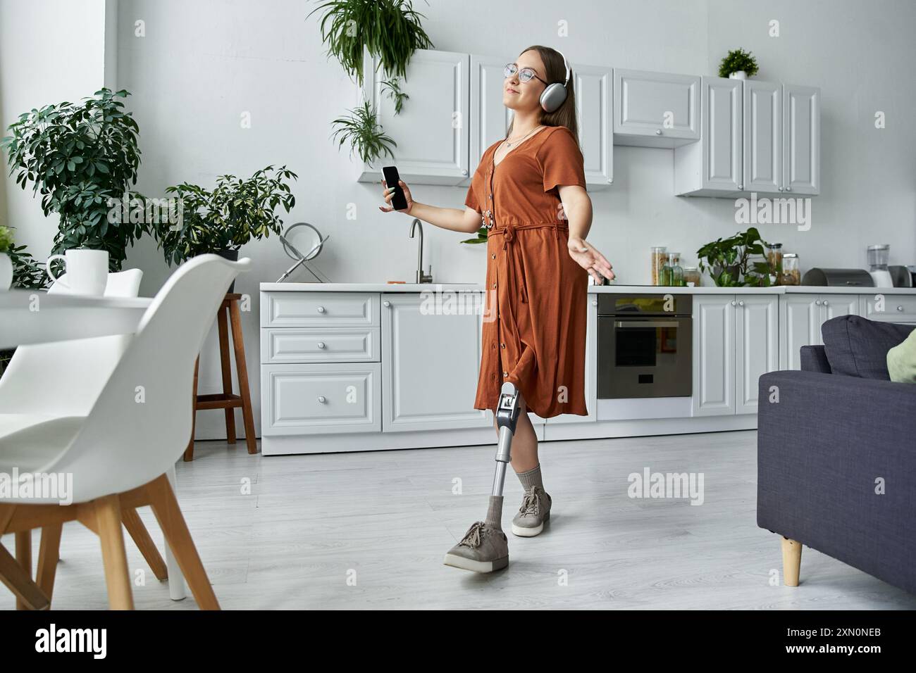 Una donna con una gamba protesica balla liberamente nella sua cucina, godendosi la musica. Foto Stock