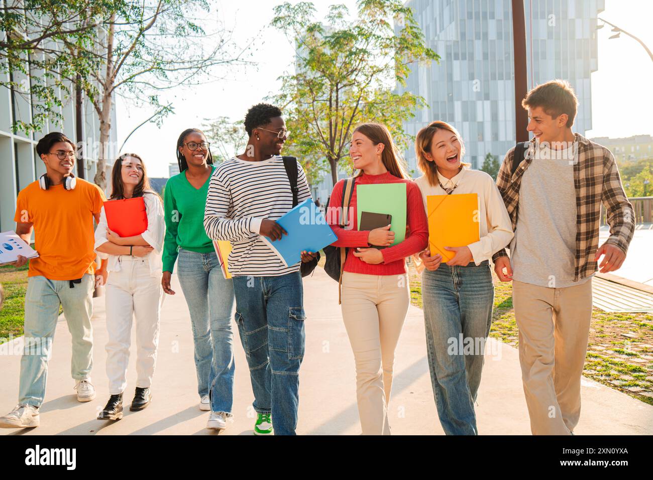 Un grande gruppo di compagni di classe internazionali che camminano e parlano insieme nel campus universitario. Felici studenti multietnici che ridono mentre vanno all'academ Foto Stock