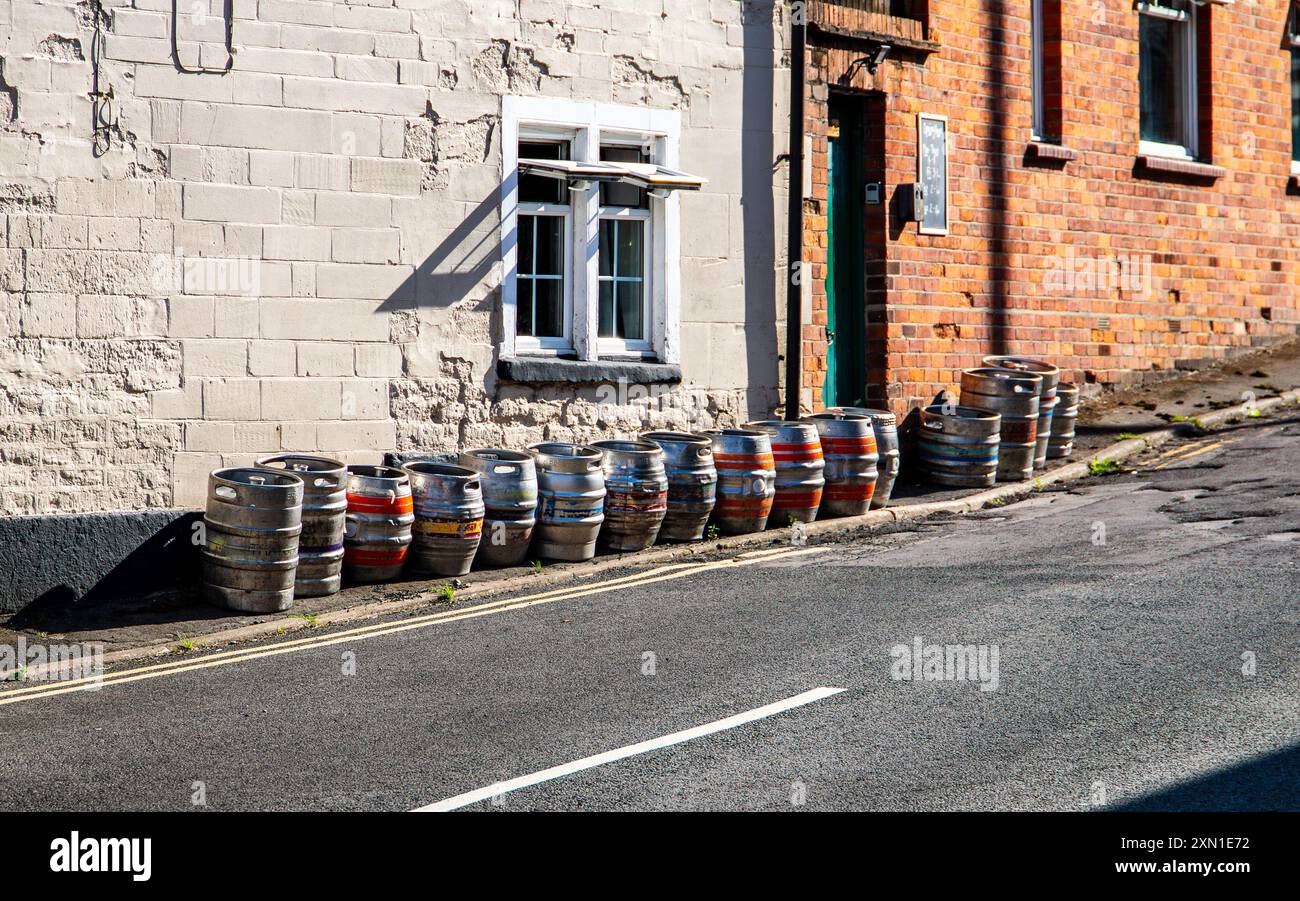 Una fila di fusti di birra vuoti allineati contro il muro esterno di un vecchio edificio lungo una strada tranquilla. Foto Stock