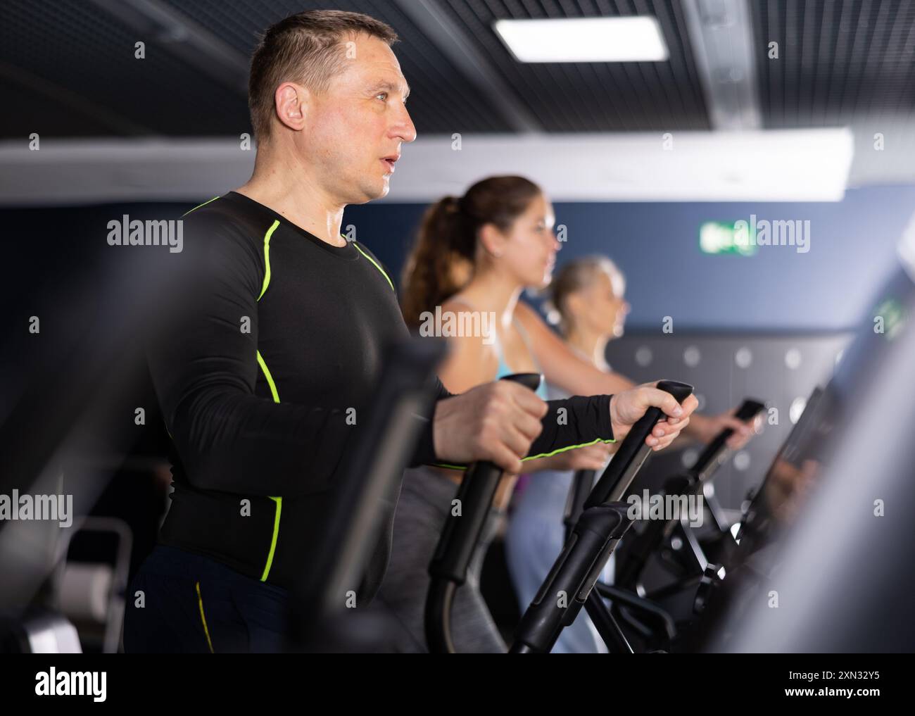 Un uomo di mezza età in palestra è impegnato in sport utilizzando un simulatore ellissoide. Stile di vita sano e concetto di sport Foto Stock