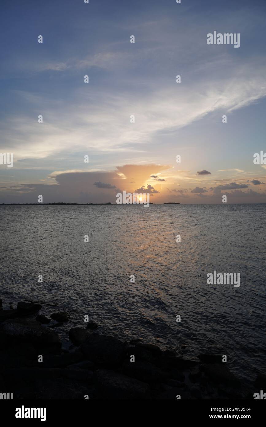 Un incantevole tramonto dorato su un oceano tranquillo, con isole lontane che creano una splendida silhouette contro il cielo vibrante. La scena è perfetta Foto Stock