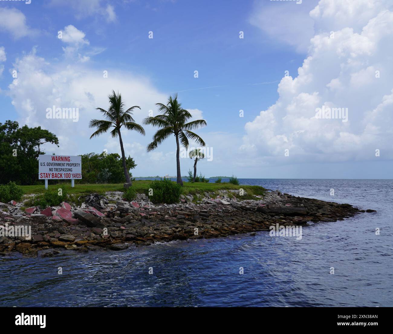 Una tranquilla scena costiera con palme sulla riva e un cartello indicante «proprietà del governo degli Stati Uniti, no Trespassing» Foto Stock