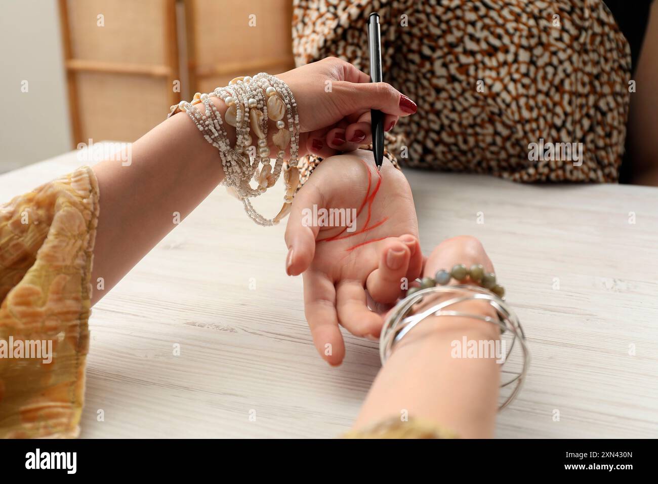 Il cassiere della fortuna legge le righe sulla palma della donna al tavolo di legno bianco, primo piano. Chiromancy Foto Stock