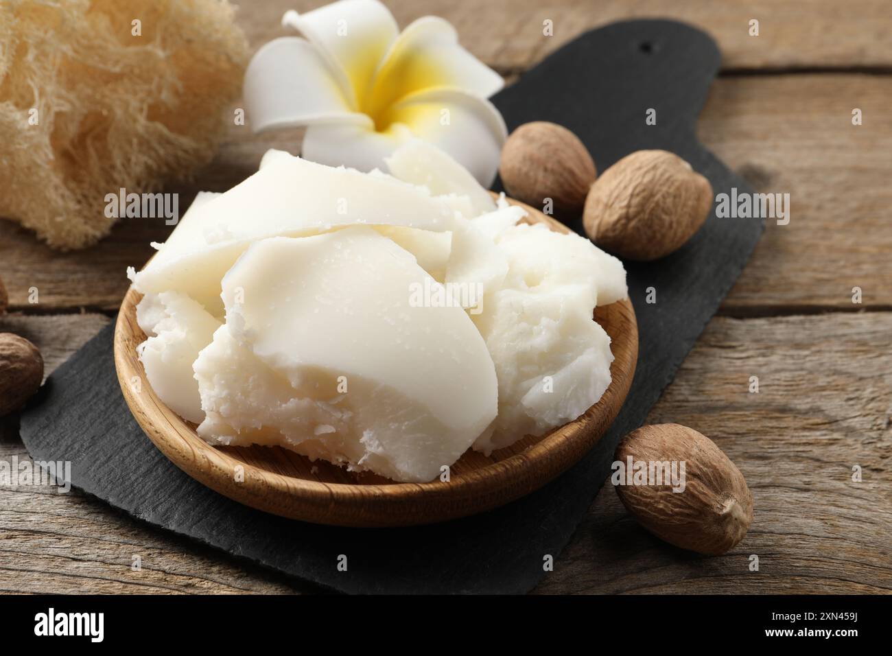 Burro di karité naturale, noci, fiori di plumeria e spugna di loofah su tavola di legno Foto Stock