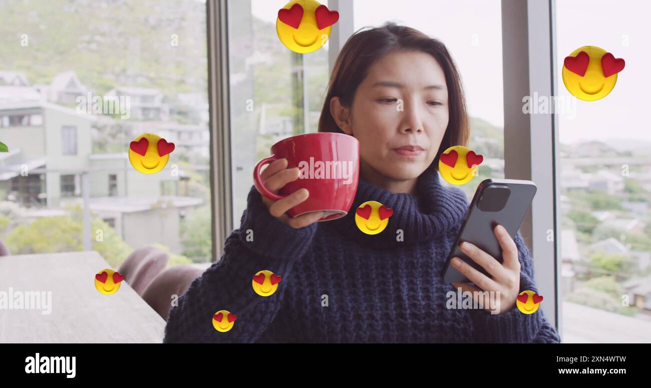 Immagine di icone emoji sulla donna asiatica che beve caffè e usa lo smartphone a casa Foto Stock