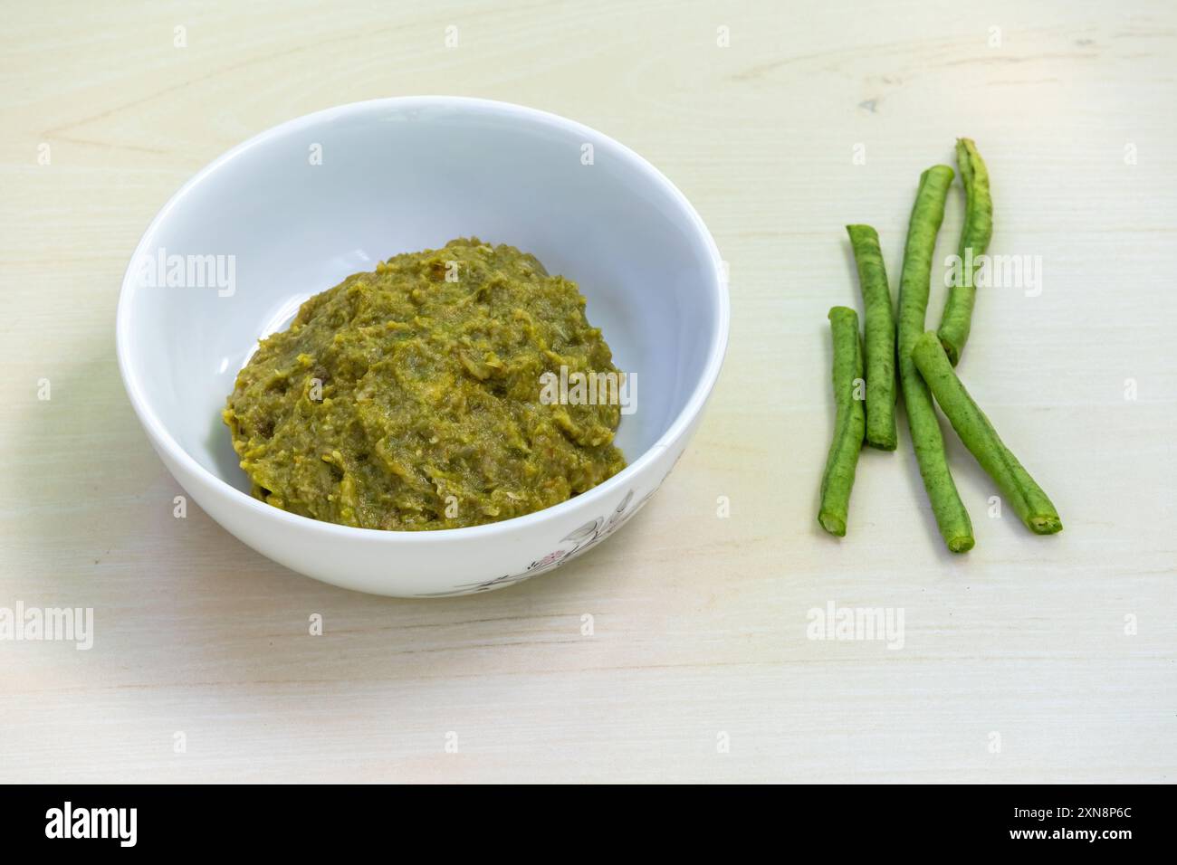 Borboti bhorta in una ciotola bianca su fondo di legno, fagioli lunghi tagliati o fagioli di asparagi posti accanto. È vegetale sano e anche conosciuto come Foto Stock