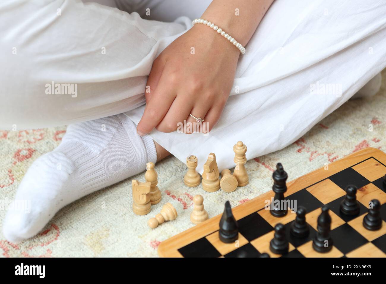 Ragazza che gioca a scacchi seduta sul pavimento - concetto capacità di pensiero capacità decisionale strategia mossa successiva braccialetto a mano anelli pezzi scacchi Foto Stock