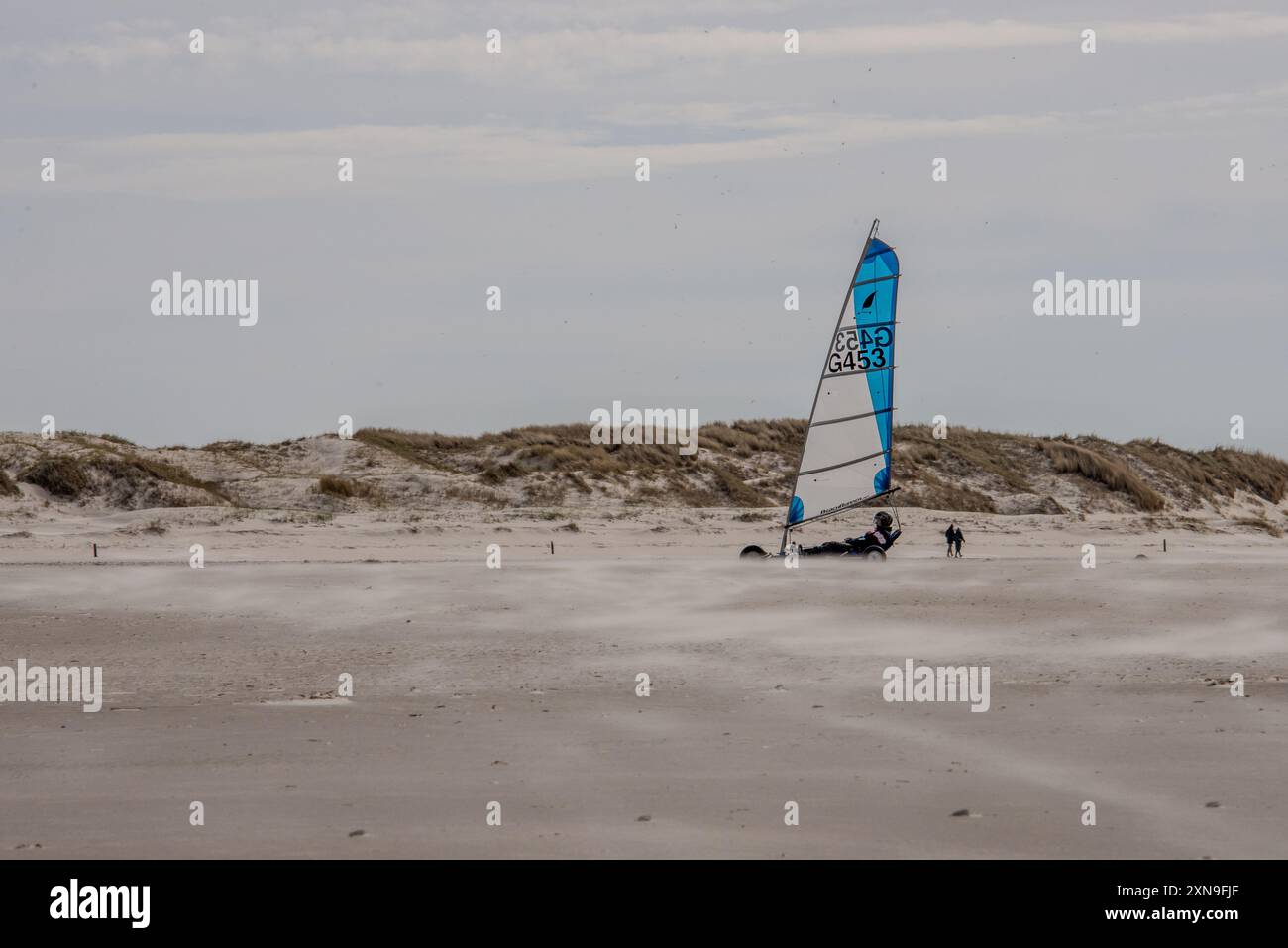 Uno yacht di terra che corre sulle sabbie piatte della spiaggia di Sankt-Peter-Ording. La navigazione a terra è uno sport popolare in questa località balneare sulla costa tedesca del Mare del Nord. Un vento costante sta guidando nuvole di sabbia e polvere attraverso le distese di marea. Foto Stock