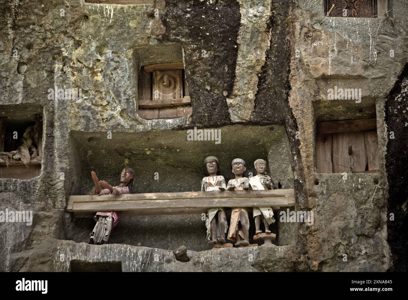 Aperture di tombe in pietra e effigi in legno su una scogliera in un tradizionale luogo di sepoltura a Lemo, Nord Toraja, Sud Sulawesi, Indonesia. Foto Stock