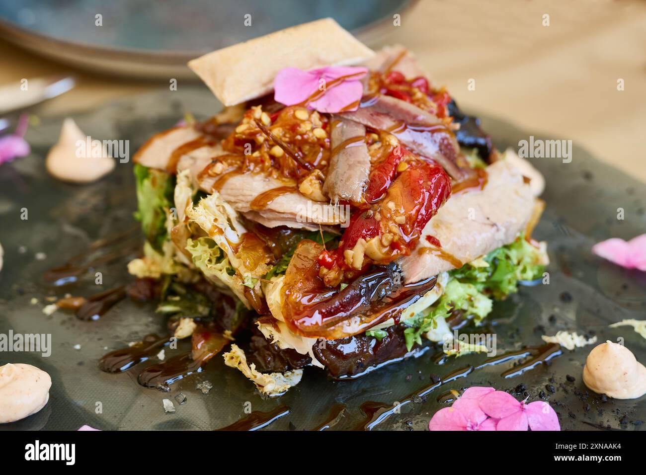 Insalata di pancia di tonno con peperoni rossi, noci e varie lattughe su un piatto di vetro, condita con aceto di Modena Foto Stock