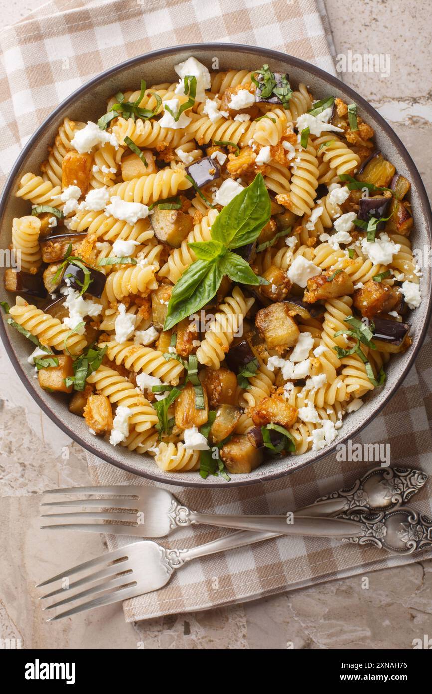 Pasta fusilli fatta in casa cotta con melanzane, aglio, feta e pangrattato da vicino in una ciotola sul tavolo. Vista dall'alto verticale Foto Stock