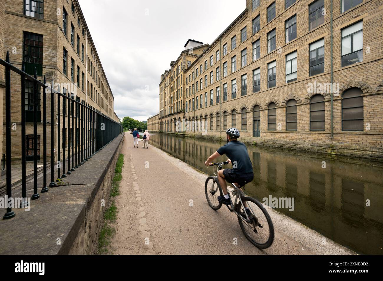 Un ciclista sul sentiero del canale Leeds-Liverpool a Salts Mill, Saltaire, un sito Patrimonio dell'Umanità, West Yorkshire, Regno Unito Foto Stock