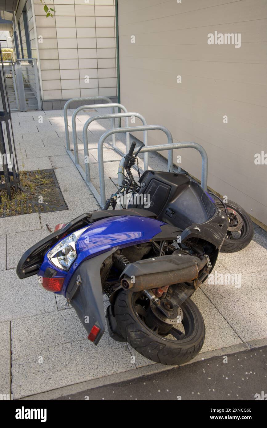 Scooter blu con fili rotti lasciati dietro giacendo sul lato vicino al parcheggio delle biciclette; a quanto pare qualcuno ha cercato di rubarlo tirando i fili Foto Stock