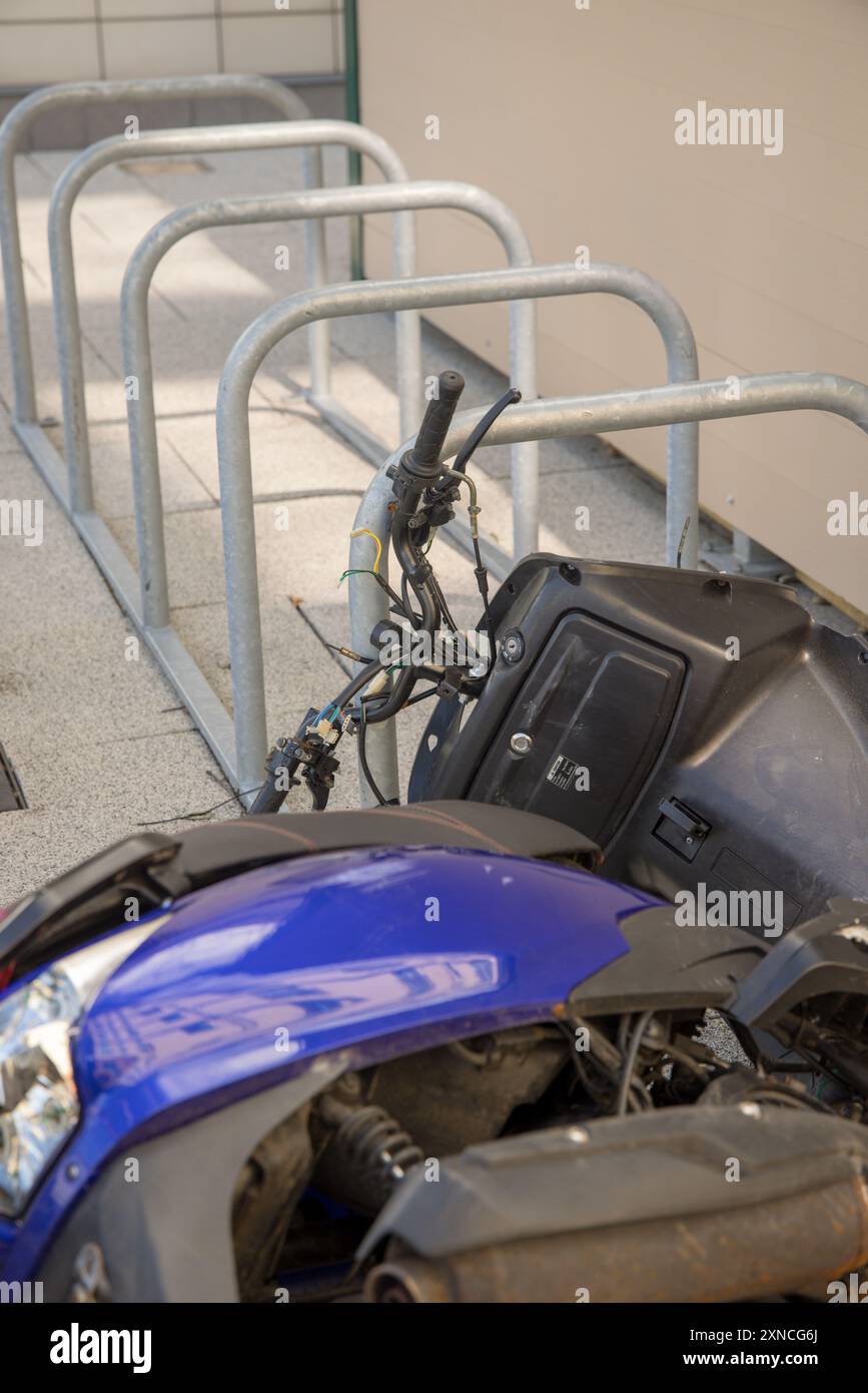 Scooter blu con fili rotti lasciati dietro giacendo sul lato vicino al parcheggio delle biciclette; a quanto pare qualcuno ha cercato di rubarlo tirando i fili Foto Stock