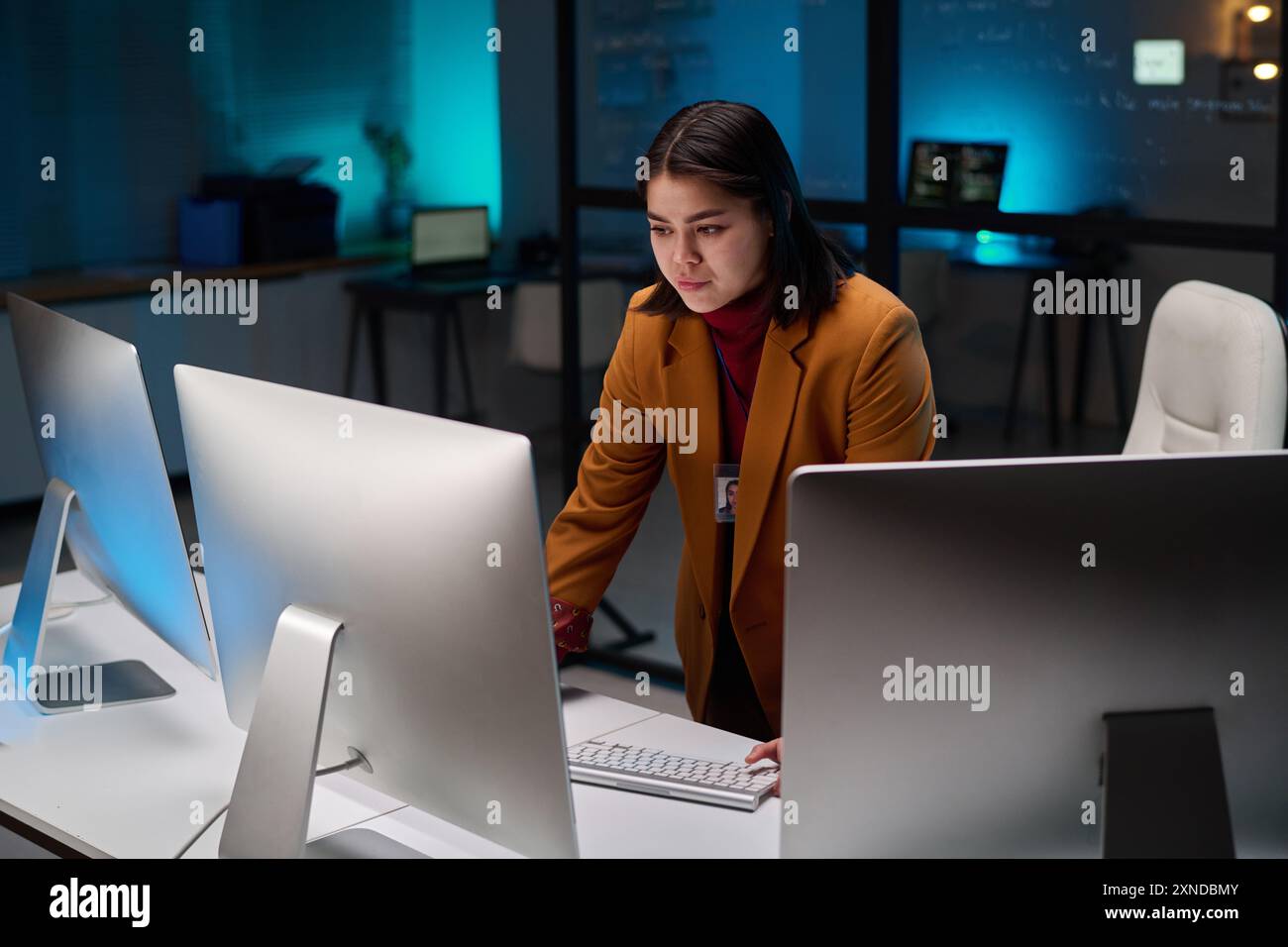 Ritratto di una donna esperta di sicurezza informatica che utilizza un computer con più monitor in ufficio illuminati da luce blu Foto Stock