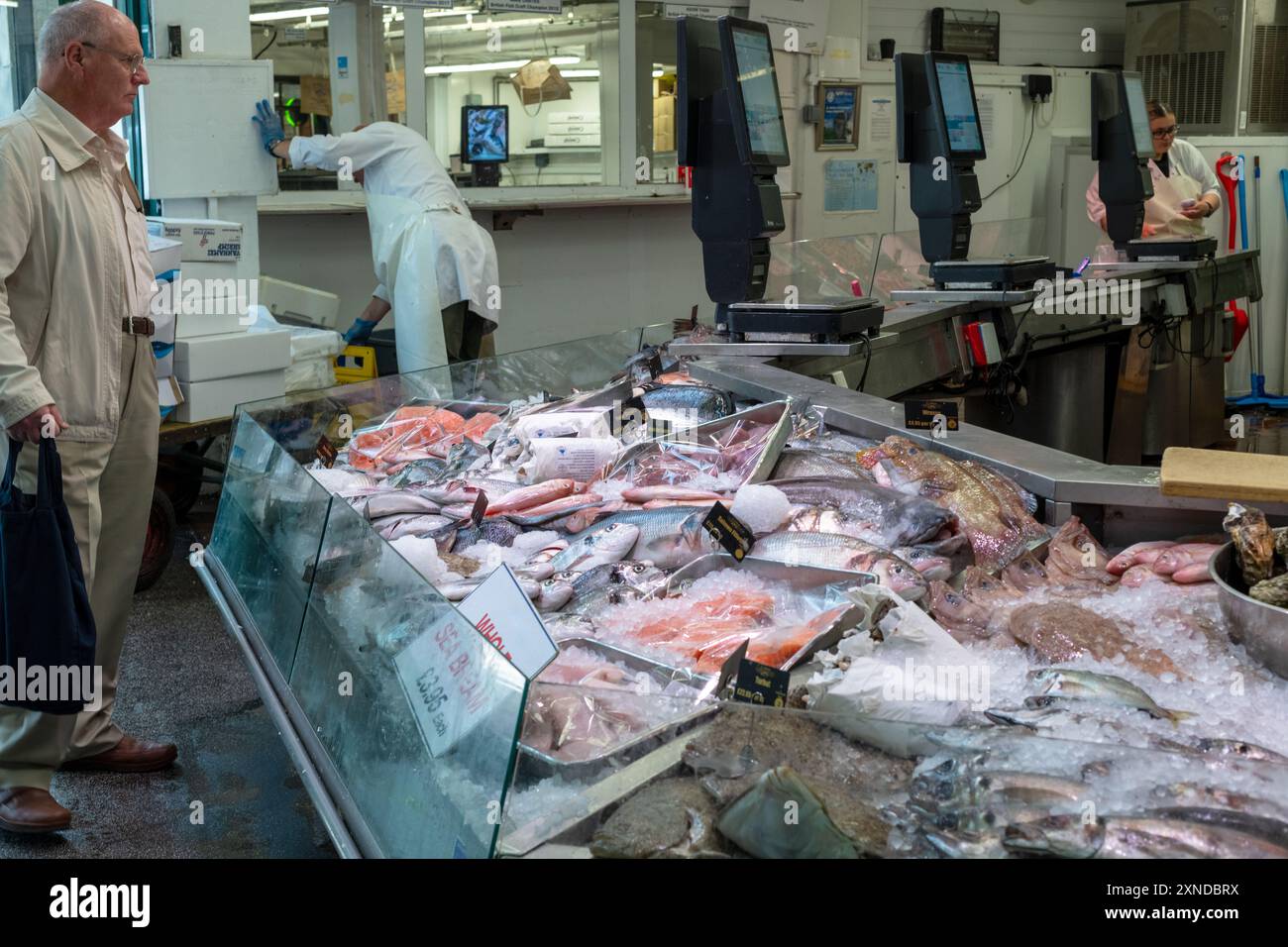 Un pensionato con una borsa della spesa attende di essere servito presso la ben rifornita bancarelle di pesce del mercato di Cardiff, Regno Unito 30/07/2024 Foto Stock