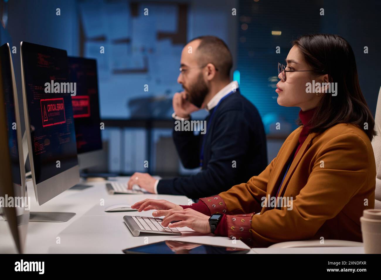 Immagine laterale di una giovane donna come programmatrice di computer che lavora fino a tardi nel dipartimento di sicurezza informatica illuminata dalla luce blu Foto Stock