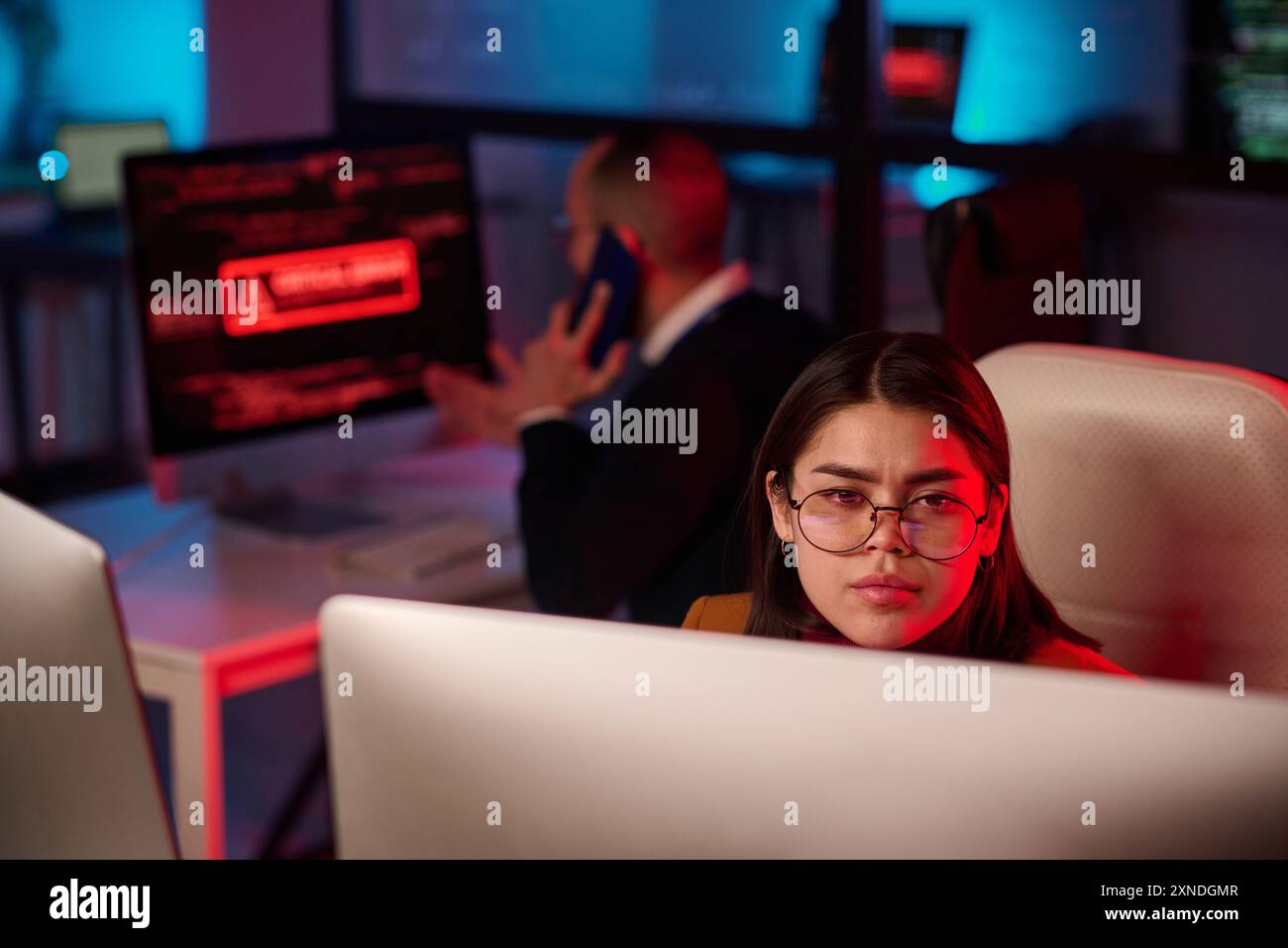 Ritratto di giovane donna che indossa occhiali e guarda lo schermo del computer nel dipartimento di sicurezza informatica con spazio di copia luce di emergenza rossa Foto Stock