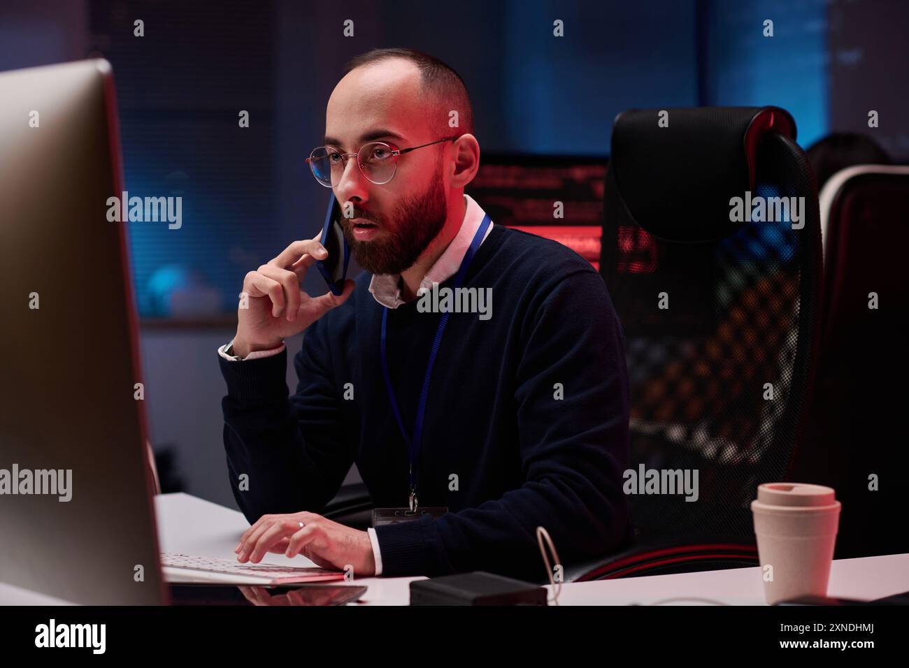 Ritratto di un uomo adulto che usa il computer e parla al telefono mentre lavora su emergenza nello spazio di copia del dipartimento di sicurezza informatica Foto Stock