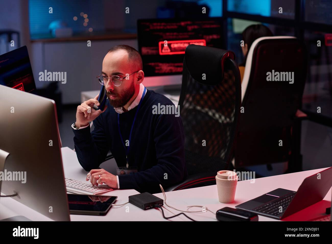 Vista ad angolo alto per un adulto con barba che utilizza un computer con più monitor nel reparto di sicurezza informatica e parla al telefono Foto Stock
