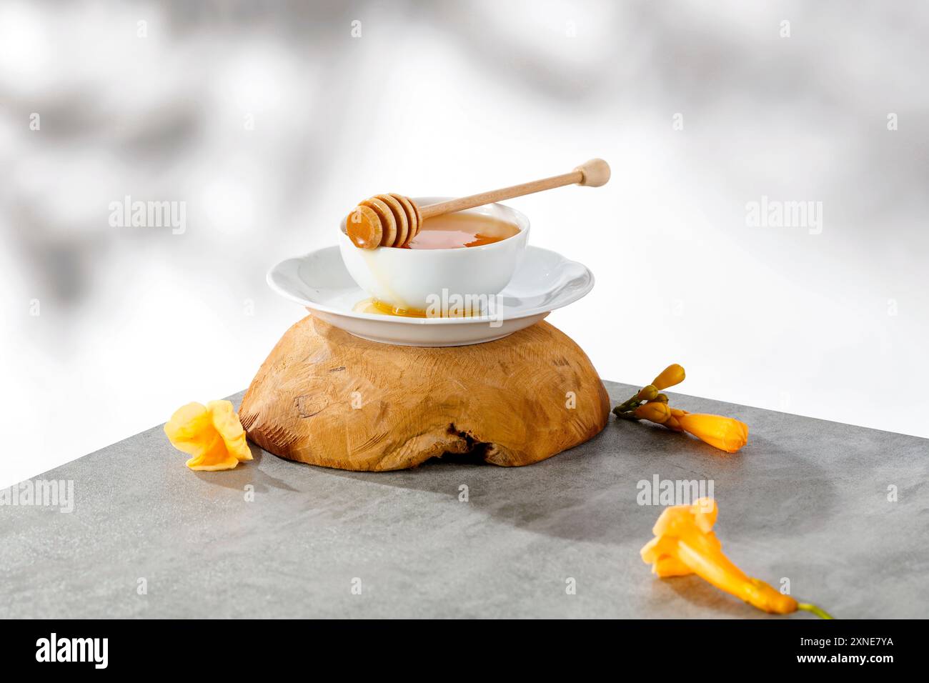 Ciotola bianca di miele e cucchiaia di miele e lavanda su un panno da cucina su un tavolo grigio con sfondo alla luce del sole. Foto Stock
