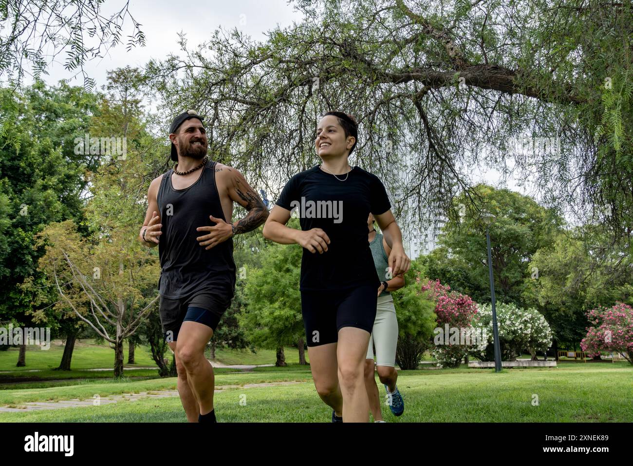 Un gruppo diversificato di persone si vede correre attraverso un vivace parco urbano verde, rimanendo in salute e in forma Foto Stock