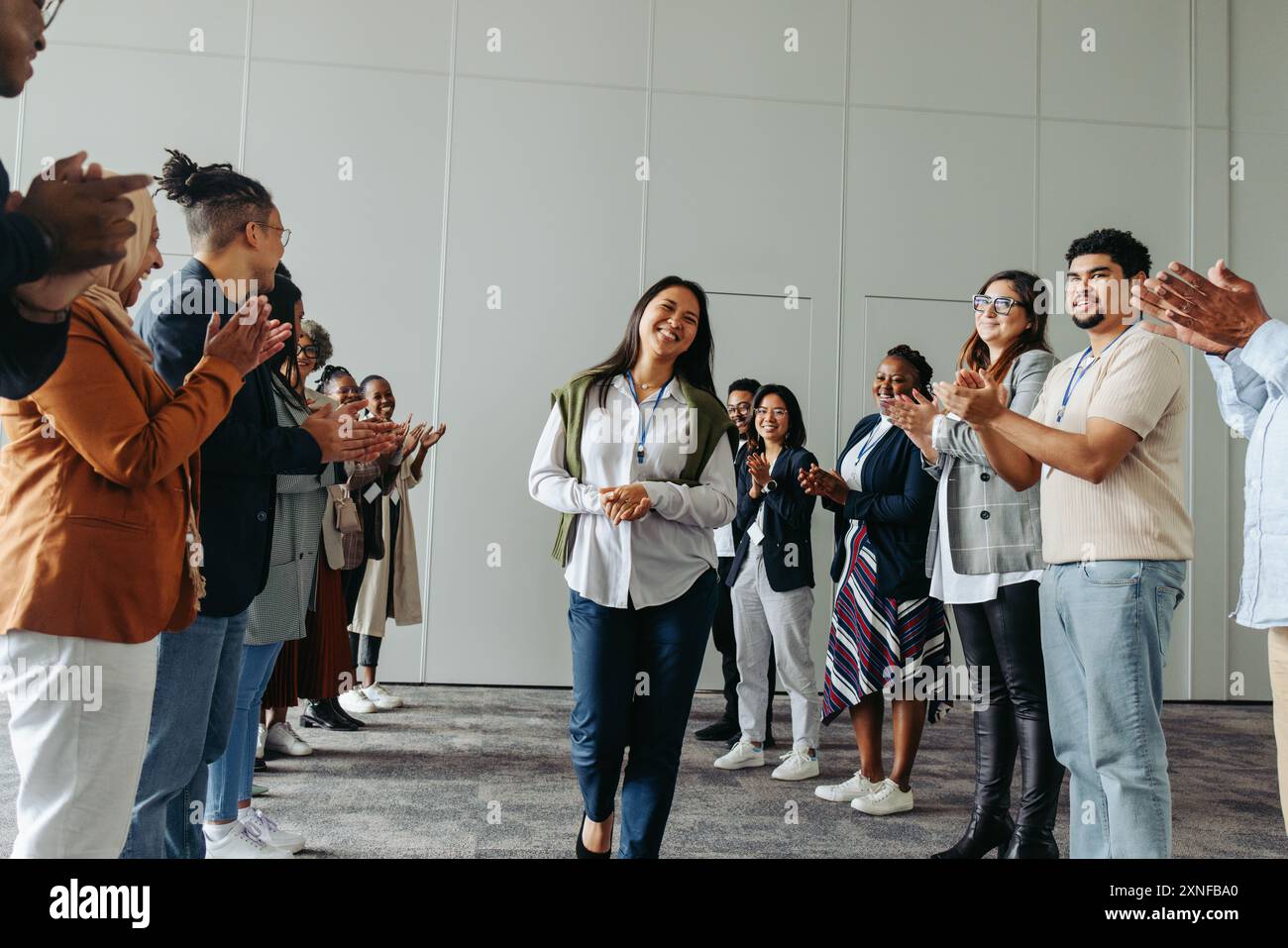 Diversi gruppi di dipendenti che battono e sorridono in una conferenza di lavoro, evidenziando un momento di festa e di successo con particolare attenzione alle donne Foto Stock
