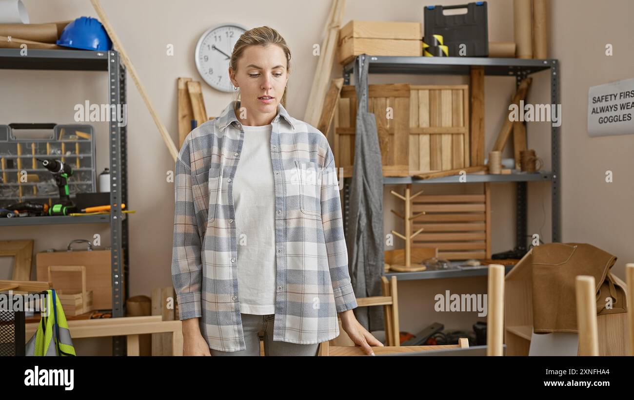 Una giovane donna pensiva si trova in un'officina di falegnameria ben attrezzata, circondata da utensili per la lavorazione del legno. Foto Stock