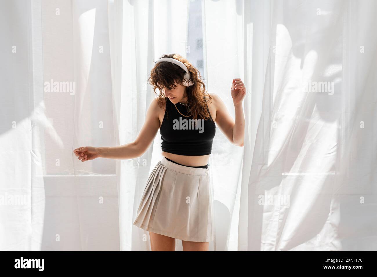 la donna balla davanti alla finestra mentre ascolta la musica con le cuffie. Foto Stock