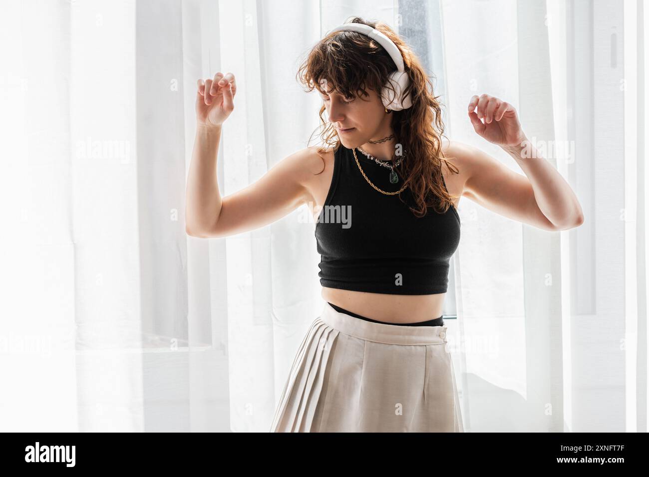 la donna balla davanti alla finestra mentre ascolta la musica con le cuffie. Foto Stock