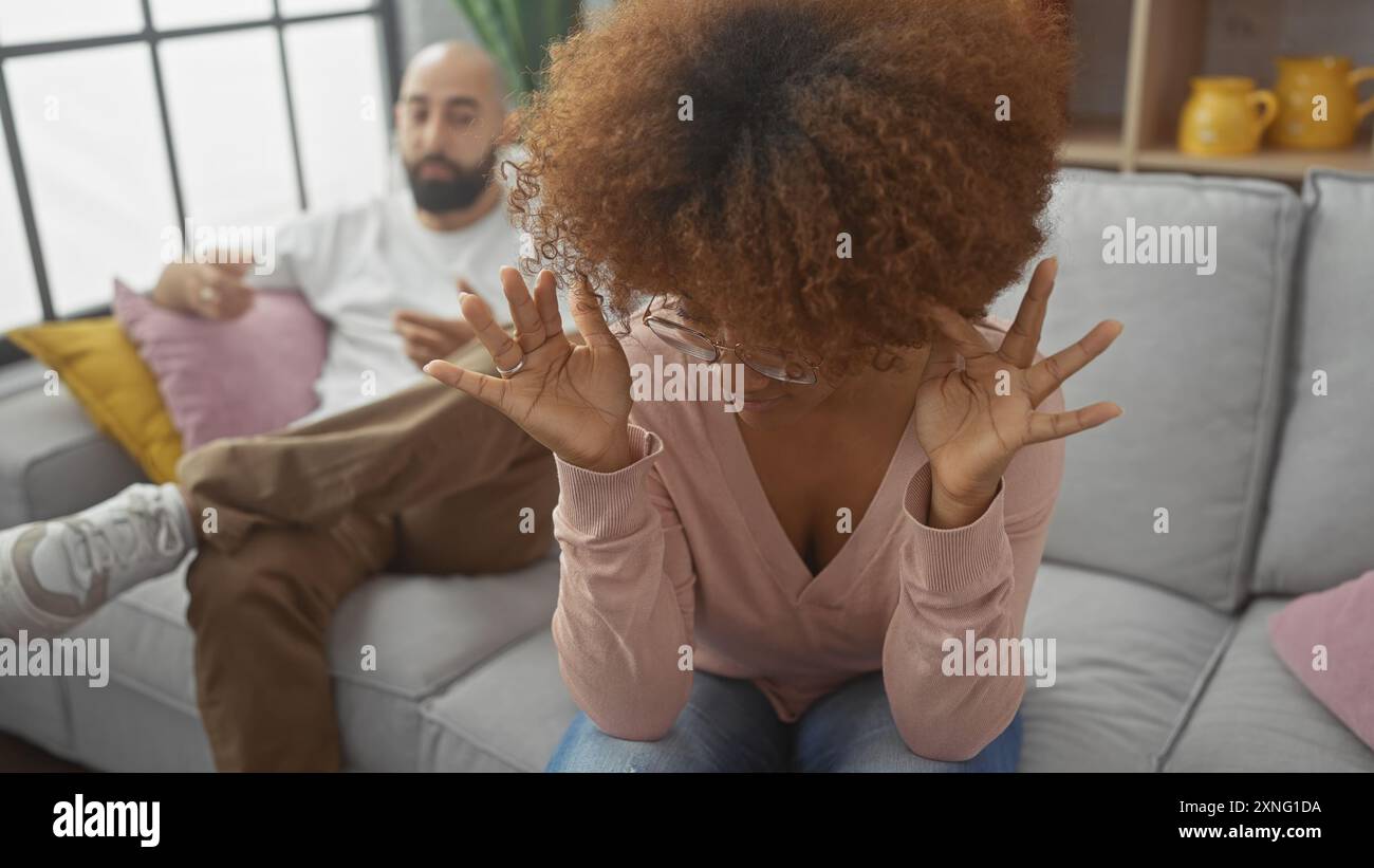Una donna turbata gesta frustrazione durante una discussione con un uomo seduto su un divano in un salotto moderno. Foto Stock
