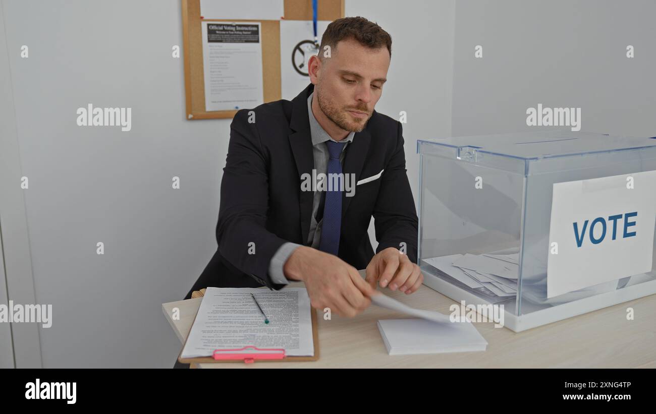 Un uomo professionista in tuta sta facendo un voto in una casella di voto in un college elettorale al chiuso. Foto Stock