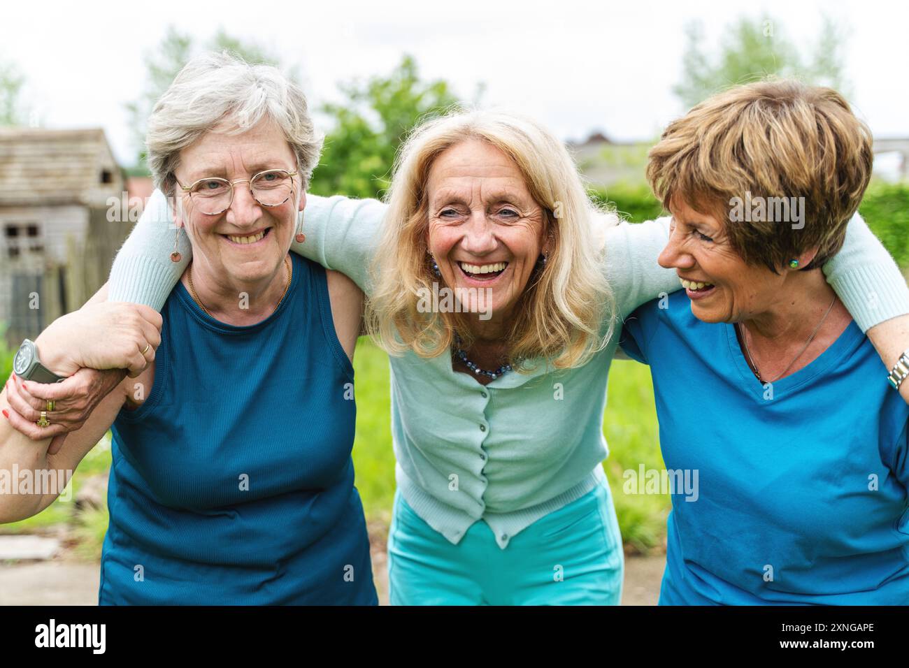 Tre donne anziane che condividono un momento intimo di risate e connessione in un giardino. Catturare l'amicizia genuina, il legame emotivo e la gioia di Foto Stock