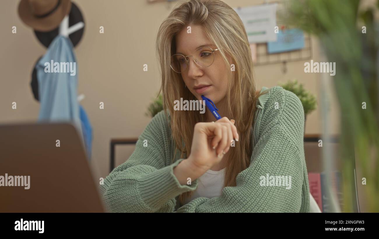 Una giovane donna con un maglione che lavora da casa, i suoi occhiali e l'espressione premurosa indicano concentrazione e determinazione. Foto Stock
