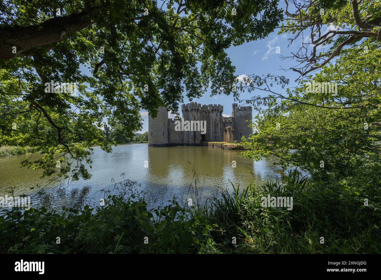 Castello di Bodiam nell'East Sussex, Inghilterra, incorniciato da una vegetazione lussureggiante e riflesso nel fossato circostante in una soleggiata giornata estiva. Foto Stock