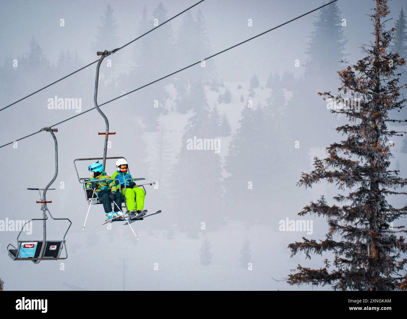 Due bambini che si godono un giro panoramico in seggiovia in alto nel cielo. Foto Stock