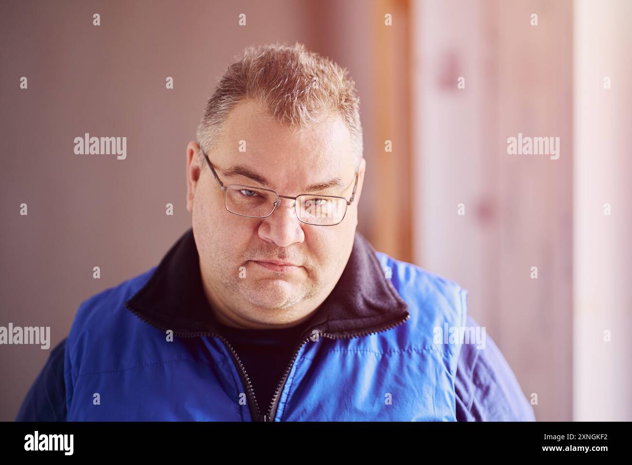 Un grande uomo dalle guance grintose del gruppo etnico caucasico con occhiali da vista ha un aspetto squallido da sotto le sopracciglia. Foto Stock