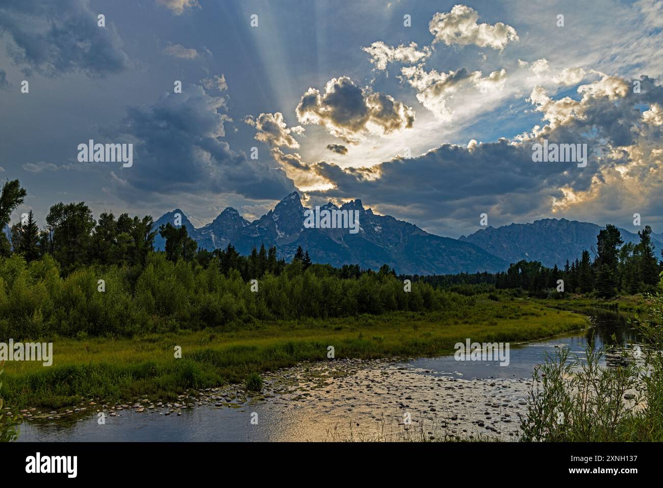 Il sole tramonta tra le nuvole dietro il Grand Teton Peak nella Teton Range del Grand Teton National Park, Teton County, Wyoming, Stati Uniti. Foto Stock