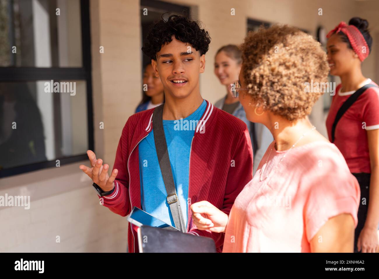 Adolescente che parla con l'insegnante, tiene un tablet, cammina nel corridoio della scuola superiore Foto Stock