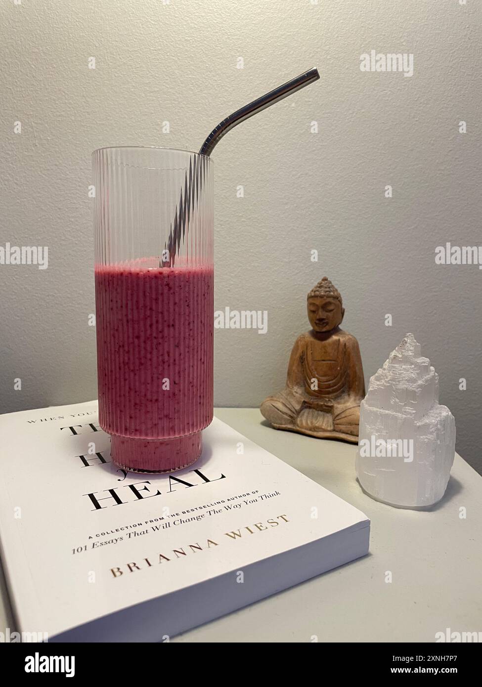 Frullato sano posto sopra un libro con statuette di Buddha. Perfetto per il benessere, la vita sana e temi di consapevolezza. Foto Stock