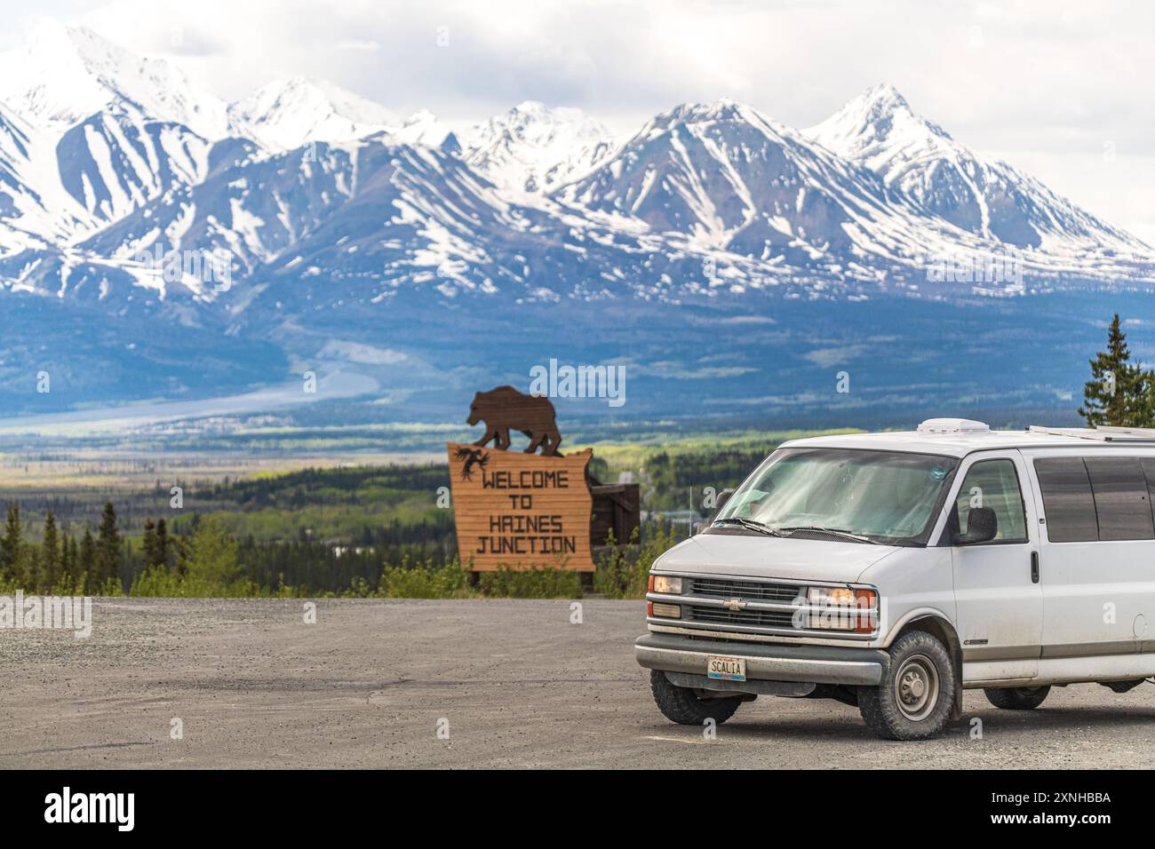 Vista primaverile di Haines Junction nell'area canadese settentrionale con cartello di benvenuto con un orso e un enorme sfondo innevato Foto Stock