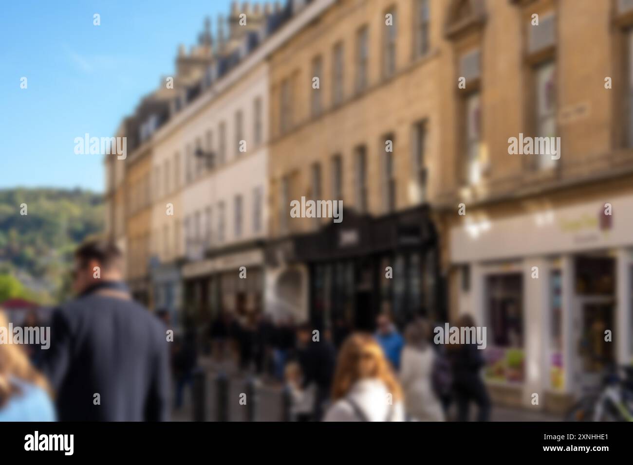 Un'immagine sfocata di una strada trafficata a Bath, nel Regno Unito, con gente che cammina davanti alle finestre del negozio e un cielo azzurro. Foto Stock