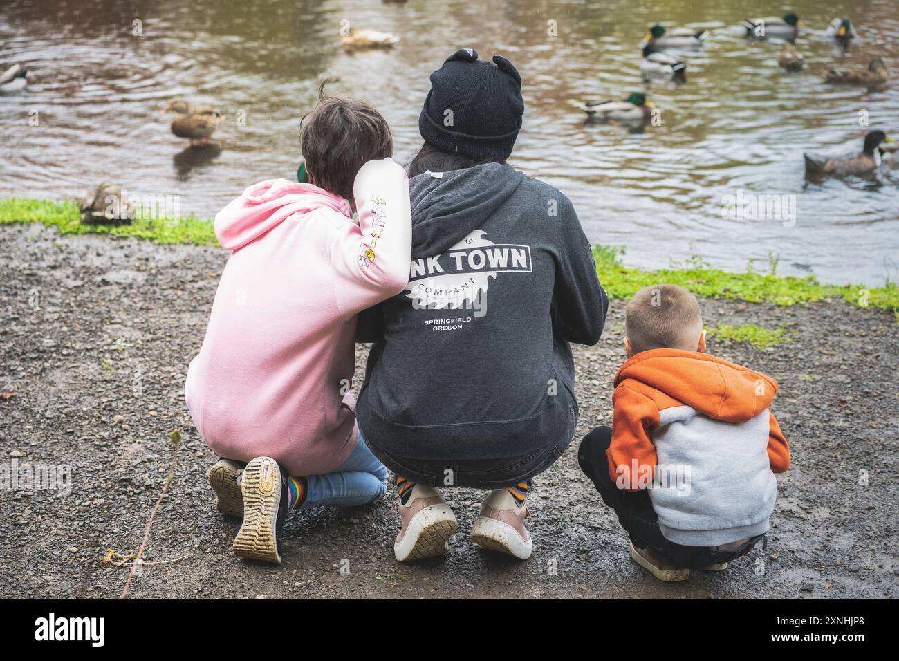 una famiglia di tre persone che si accovacciano per guardare le anatre in uno stagno Foto Stock