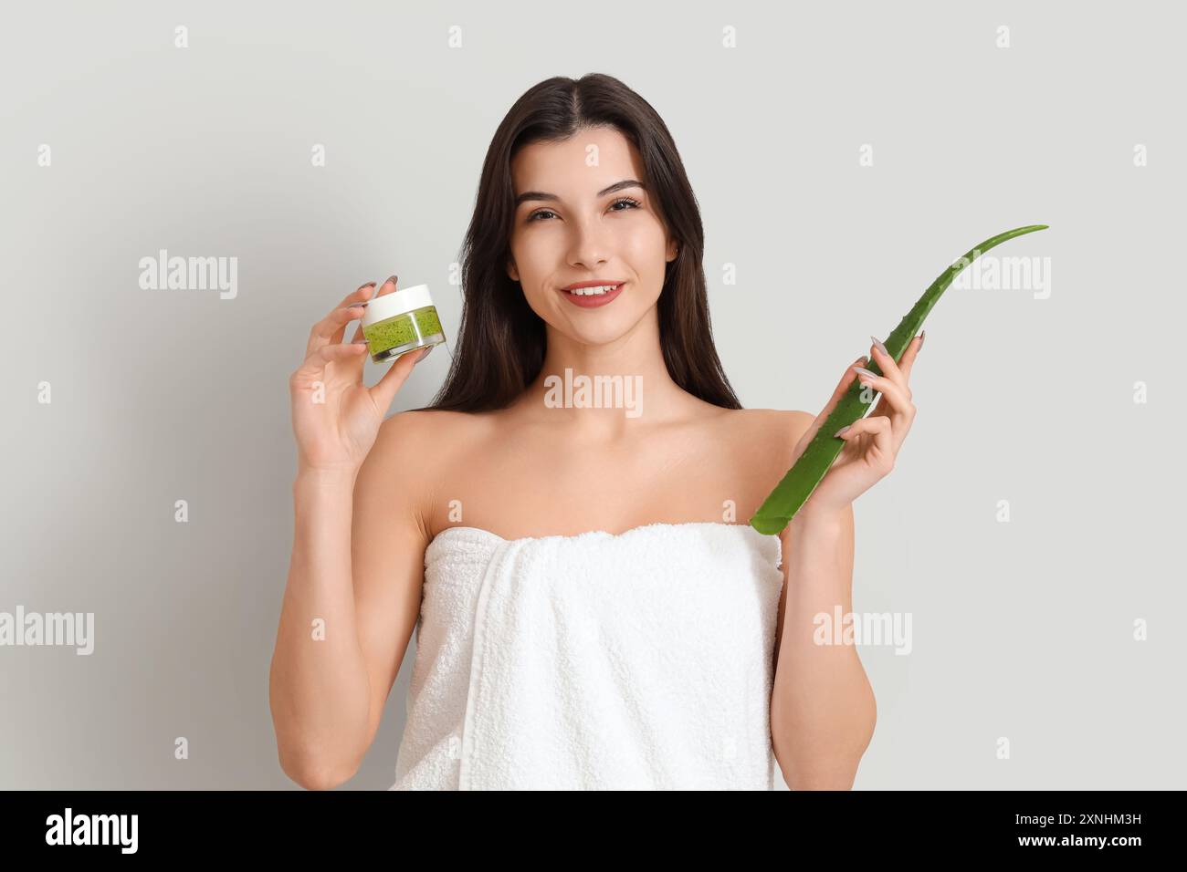 Bella giovane donna felice con foglia di pianta e vaso di gel di aloe vera su sfondo grigio Foto Stock