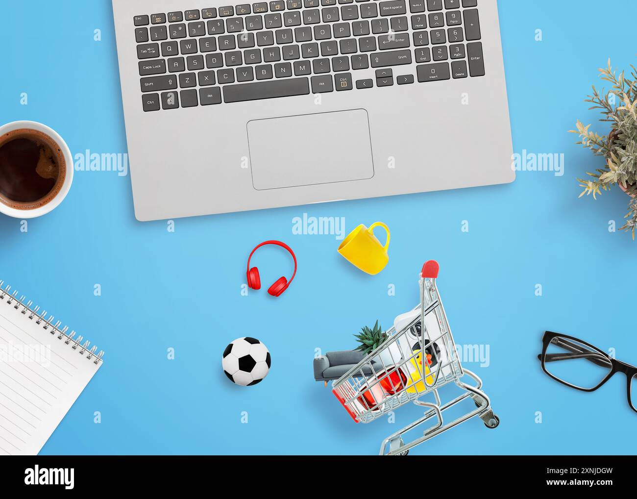 Carrello della spesa su una scrivania con prodotti intorno e un computer portatile accanto. Concetto di shopping online e retail digitale Foto Stock
