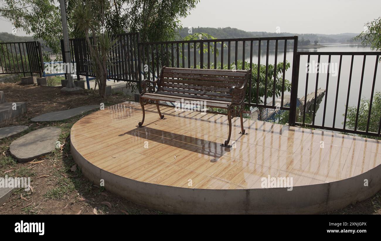 Panca da giardino in metallo marrone sopra la piattaforma piastrellata lucida con vista sul lago. Ideale per pubblicità di mobili per esterni, brochure di giardini, paesaggi. Foto Stock