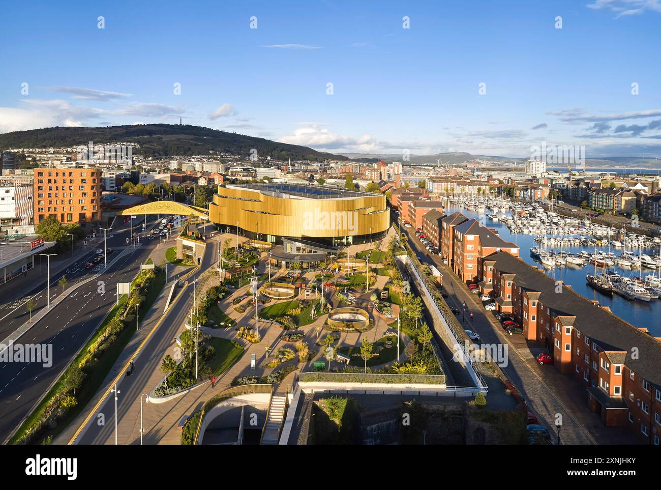 Vista aerea del porticciolo, del ponte e dell'arena illuminata dal sole. Swansea Arena e Copr Bay Bridge, Swansea, Regno Unito. Architetto: acme, 2024. Foto Stock